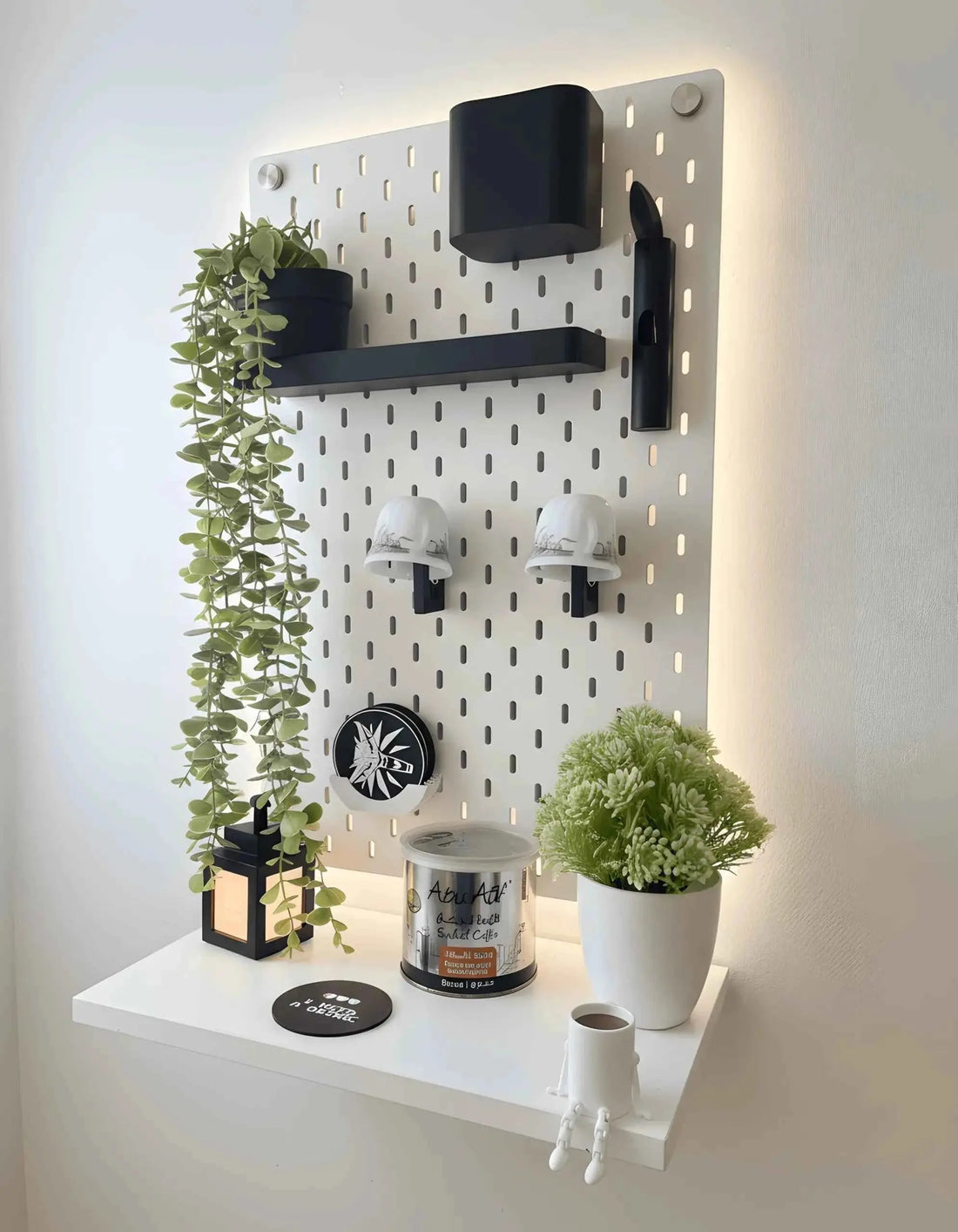 Pegboard-mounted coffee station with mug hooks and a cup shelf beside a desk