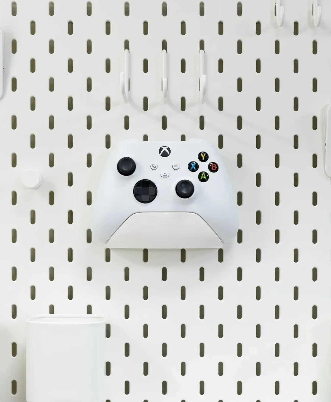 Pegboard wall holding a headset, controller and keyboard on wall-mounted holders